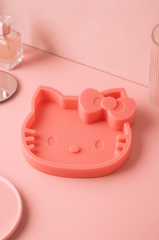 Pink catch all tray mat shaped like a cat's face with a bow on a pink surface.